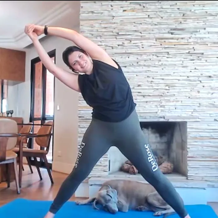 Lívia DeRose fazendo uma flexão lateral do tronco, em pé, em casa